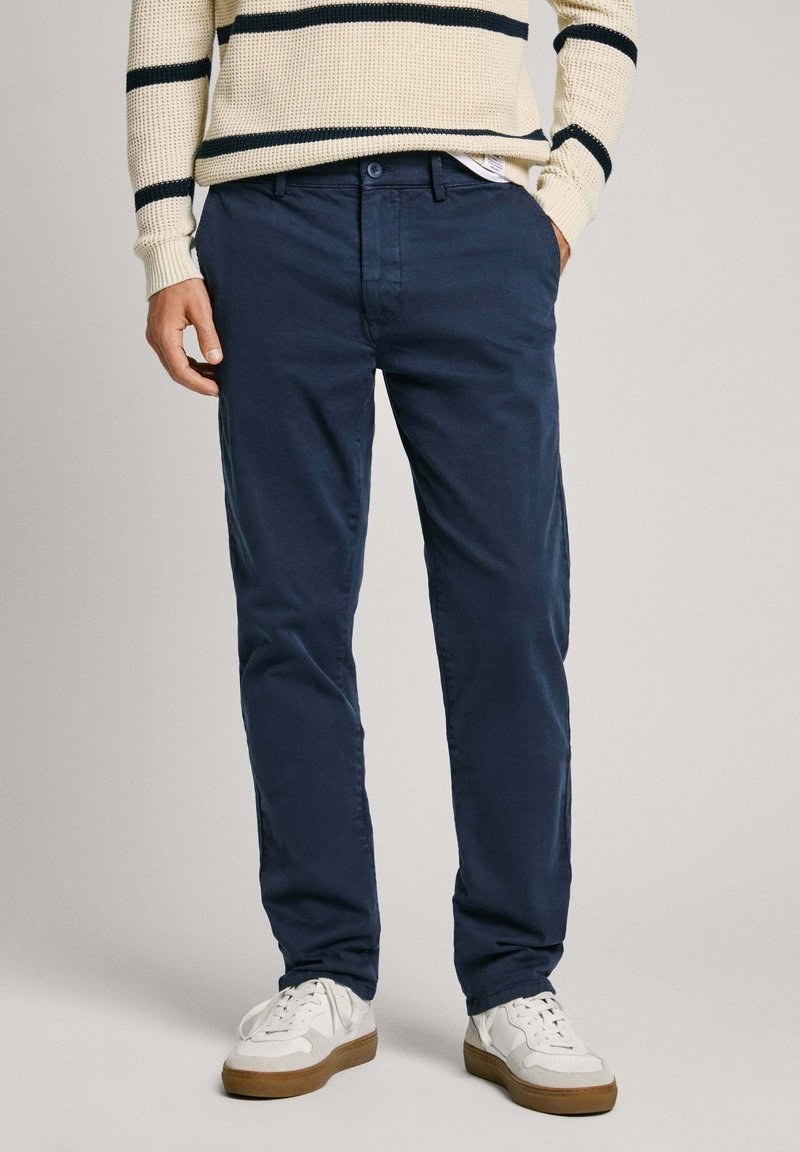 Tamsiai mėlynos medvilninės chinos kelnės su tiesiu siluetu, turinčios šonines kišenes ir sagos užsegimą. Derinamos su baltomis sportinėmis bateliais ir kreminės spalvos dryžuotu megztiniu.