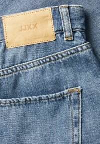 Jeans in denim con un lavaggio azzurro chiaro, cuciture gialle a contrasto e una patch in pelle beige con "JJXX" impressa sulla vita.