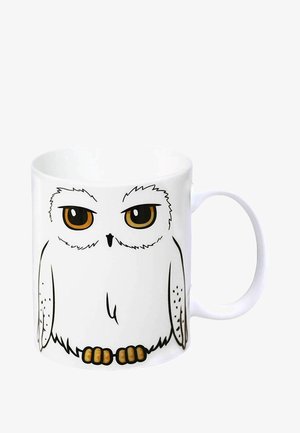 Weißer Keramikbecher mit einem Eulendesign im Cartoon-Stil. Die Eule hat große braune Augen und einen runden Körper mit orangefarbenen Füßen, die in Schwarz umrandet sind.