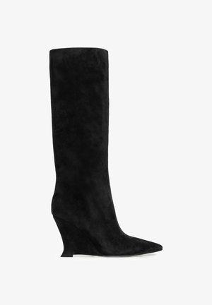Černé semišové kotníkové kozačky na klínovém podpatku sahající až ke kolenu, s špičatou špičkou a vysokým zakřiveným podpatkem, zobrazené ze strany na bílém pozadí.