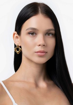 Goldene Ohrringe mit einem geometrischen, skulpturalen Design; sie besitzen eine markante rautenförmige Kontur und eine polierte Oberfläche.