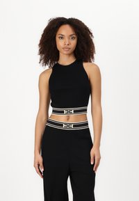 Melna īsa topa blūze ar augstu apkakli, kurai ir kontrastējoša balta svītraina jostas daļa un logotipa elements. Gluda adījumus audums.