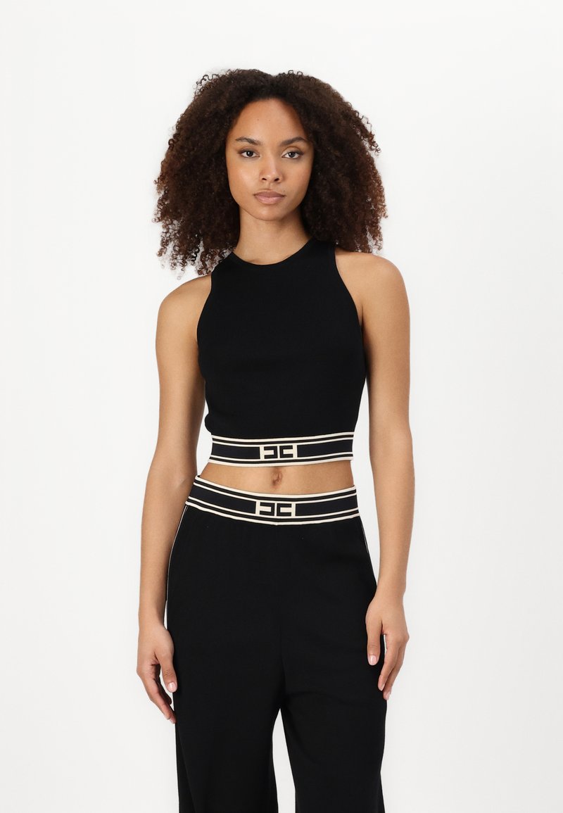 Melna īsa topa blūze ar augstu apkakli, kurai ir kontrastējoša balta svītraina jostas daļa un logotipa elements. Gluda adījumus audums.