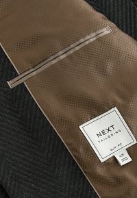 Podszewka kurtki o kroju slim w ciemnobrązowym kolorze z teksturowanym wzorem, wyposażona w kieszeń na zamek i oznaczona metką "NEXT TAILORING".