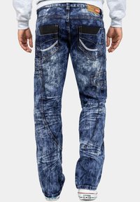 Jeans in denim blu con una finitura consumata, caratterizzati da tasche a contrasto nere, una vestibilità slim e dettagli di cucitura in vista.