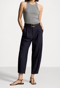 Grå ribbad linne, högmidjade marinblå byxor med veck, svart bälte med guldspänne, och svarta platta sandaler.