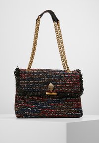 Tweed håndtaske med sort frynse, flerfarvet mønster i rød, blå og brun, guld kædetræk og guld håndformet lås på hvid overflade.
