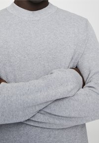 Gray knitted sweater with a ribbed texture, featuring a crew neck and long sleeves, showcased with arms crossed.