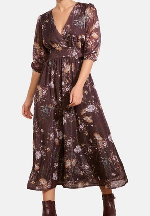 Donna che indossa un vestito midi marrone a fiori con maniche a tre quarti a sbuffo e scollatura a V profonda.