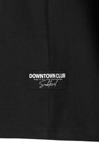 Black cotton t-shirt featuring a rectangular label with white text that reads "DOWNTOWN CLUB RISK IT ALL FOR YOUR PASSION Sublevel."