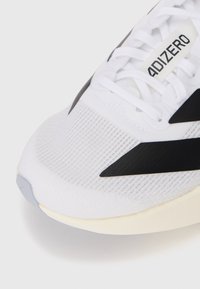 Close-up of a white running shoe with black stripes, mesh upper, and white laces, featuring "ADIZERO" text on the tongue.
