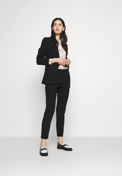 Blazer aderente nero e pantaloni abbinati a una blouse a fantasia e mocassini neri con accenti bianchi. Tessuto liscio, forma su misura.