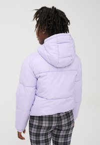 Giacca a vento lilla con cappuccio, caratterizzata da un design trapuntato e polsini elasticizzati, abbinata a pantaloni scozzesi in bianco e nero.