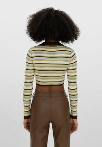 Odsłonięty top crop z długimi rękawami w jasnoniebieskim, kremowym i brązowym kolorze. Posiada prążkowaną fakturę i okrągły brązowy dekolt. Połączony z brązowymi spodniami.