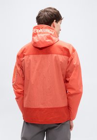 Κόκκινο μπουφάν με κουκούλα, από υφή υφάσματος, με ελαστικές μανσέτες και λογότυπο Columbia στην πλάτη. Απλός σχεδιασμός με λεπτομέρεια από διαπνέον δίχτυ.