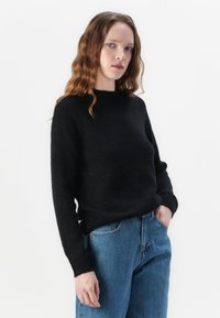 Svart stickad tröja med rund halsringning och långa ärmar, i kombination med ljusblå högmidjade jeans. Mjuk textur, minimalistisk design.