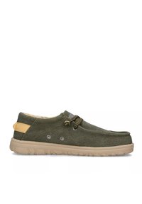 Scarpe slip-on verdi in tela con suole in gomma beige, caratterizzate da una tomaia testurizzata, lacci decorativi e un accento sul tallone in contrasto.