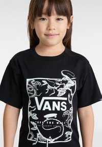 Schwarzes Baumwoll-T-Shirt mit einem weißen Grafikdruck von Dinosaurierskelette und dem "VANS Off the Wall"-Logo in der Mitte.