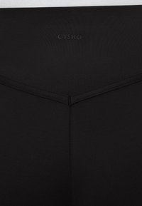 Schwarze Leggings mit einem strukturierten Bund und eingeprägtem "OYSHO"-Logo, gestaltet mit einem V-förmigen Detail auf der Rückseite.