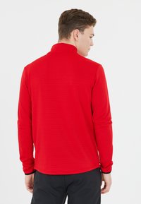 Rode langemouwen shirt met hoge kraag, met een textuurstof en een aansluitend ontwerp. De achterkant heeft een subtiel ribbelpatroon.