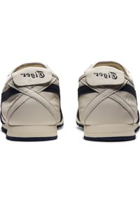 Beige leather sneakers with navy accents, rounded shape, and a textured finish. Features a logo at the heel and a padded collar.