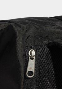 Närbild av svart tyg med en silverdragkedjehämtning som har Adidas trebladslövet och svart meshamaterial under.