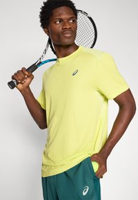 Φωτεινό κίτρινο αθλητικό μπλουζάκι με κοντά μανίκια και διάφανα ένθετα, συνδυασμένο με τιρκουάζ σορτς που διαθέτουν κρυφό τσεπάκι για μπαλάκι του τένις.