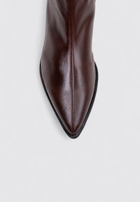 Bottine cheville en cuir marron à bout pointu avec une texture lisse et une semelle noire, présentant une couture centrale coursant le long du dessus.