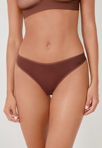 Brązowe majtki bikini o gładkiej, elastycznej fakturze i minimalnym pokryciu. Posiadają prosty, bezszwowy design oraz kontrastowy pas.