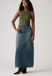 Lang denimskjørt med frontsplitt, lyseblått stoff og høy midje. Kombinert med et mørkt belte og svarte høye støvler. Olivengrønn tanktop.