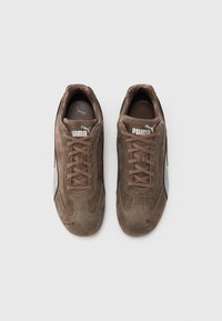 Pantofi sport maro din piele întoarsă cu finisaj texturat, prevăzuți cu închidere cu șireturi, logo Puma alb și accente întunecate pe laterale și călcâi.