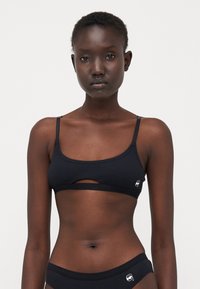 Svart ribbet bralette med smale stropper og detalj med utskjæring foran. Har en liten logo på venstre side og myk, elastisk stoff.