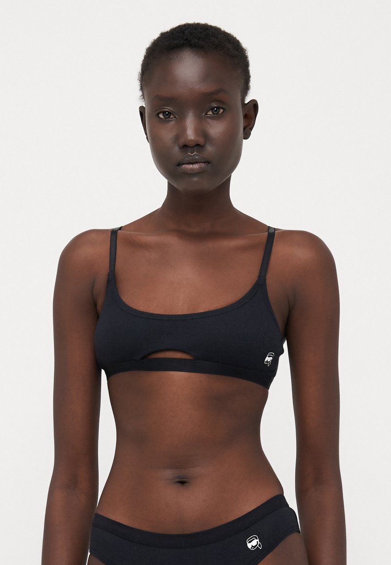 Svart ribbet bralette med smale stropper og detalj med utskjæring foran. Har en liten logo på venstre side og myk, elastisk stoff.