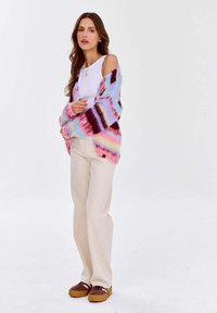 Kolorowy, oversize'owy kardigan dzianinowy z gradientem różowych, niebieskich i burgundowych pasków. Połączony z białą bluzką i beżowymi spodniami.