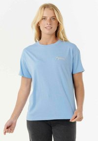 Lyseblå bomulds t-shirt med rund hals og korte ærmer. Har et lille grafisk logo trykt på venstre brystområde.