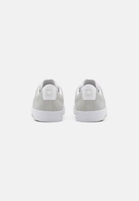 Sneaker basse in suede grigio con suole in gomma bianca e design con lacci; presenta un logo a stella bianca sul tallone e una texture liscia.