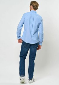 Világoskék, hosszú ujjú ing hátsó redővel, sötétkék farmerrel és fehér sportcipővel, amelyek kék és piros részletekkel rendelkeznek.