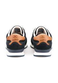 Sneakers in suede blu navy con dettagli in pelle marrone, dotati di una suola bianca e un logo in rilievo sulla parte posteriore. Texture liscia e forma arrotondata.