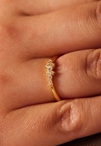 Gouden ring met een verfijnd ontwerp, versierd met meerdere kleine heldere en lichtroze kristallen die in een cluster zijn gerangschikt op een gladde band.