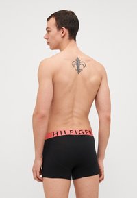 Crne bokserice s ružičastim pojasom na kojem se nalazi logo "HILFIGER". Glatka tkanina, uski kroj i minimalni detalji šivanja.