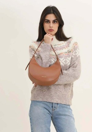 Femme portant un pull en maille à motifs et un jean, tenant un sac à main marron en forme de croissant avec le logo « cherry paris ».