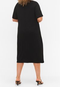 Abito midi a coste nere con maniche corte e vestibilità rilassata. Tessuto morbido, design semplice, cade sotto il ginocchio, abbinato a sandali con tacco neri.