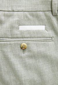 Tissu gris clair avec une finition texturée, présentant une poche plaquée et un bouton décoratif à quatre trous. Une carte blanche est visible à l'intérieur de la poche.