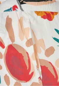 Tissu à motif floral avec de grandes formes rouges, oranges et vertes sur un fond clair. Ceinture élastique et texture lisse et légère.
