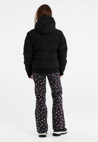 Schwarze Pufferjacke mit Kapuze, kombiniert mit dunklen gemusterten Hosen, die kleine weiße Blumen zeigen. Strukturiertes und figurbetontes Design, geeignet für kaltes Wetter.