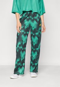 Un pantalon de sport à motif vert avec une coupe décontractée, une taille élastique et des accents noirs. Assorti avec un haut vert qui complète le tout.