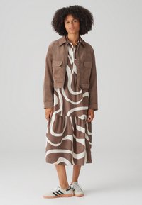 Brown cropped cord jacket with two pockets over a brown and white patterned midi dress, paired with white sneakers featuring black stripes.