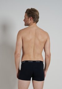 Schwarze Baumwoll-Boxershorts mit einem weißen "ceceba"-Logo auf dem elastischen Bund, getragen von einem Model, das von der Kamera abgewandt ist.