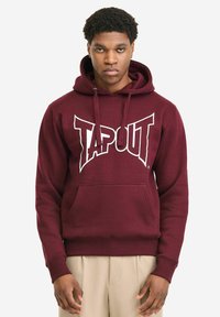 Bordo majica s kapuljačom i prednjim džepom, s bijelim logotipom "TAPOUT". Tkanina izgleda mekano s teksturiranim završetkom i rebrastim manšetama.