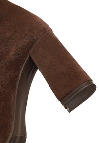 Zapato de ante marrón con tacón cuadrado, que presenta una suela de goma suave y líneas limpias. La parte superior tiene una textura suave y un diseño sin costuras.